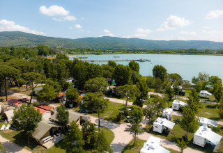 Vista aérea de Camping Punta Navaccia en Umbría, Italia, con caravanas, lago y colinas al fondo.