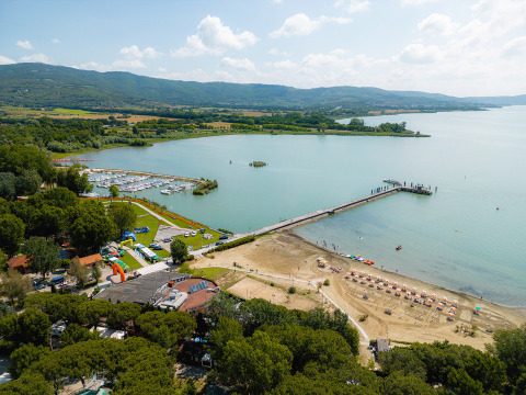 Vista aerea del Camping Punta Navaccia in Umbria, Italia, con spiaggia, pontile e marina sul lago in una giornata soleggiata.