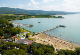 Vista aerea del Camping Punta Navaccia in Umbria, Italia, con spiaggia, pontile e marina sul lago in una giornata soleggiata.