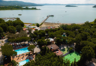 Luftaufnahme vom Camping Punta Navaccia in Umbrien, Italien, mit Pools, Sportplatz und Seeblick.
