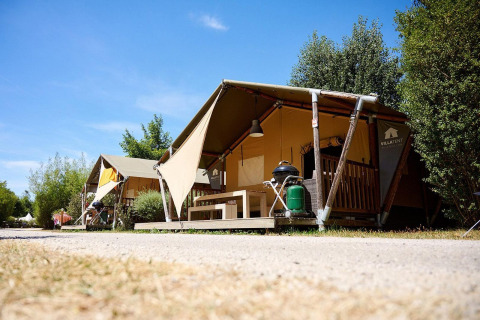Tienda safari Villatent Nomad en Camping La Roche d’Ully, Francia, con vegetación y cielo azul claro.