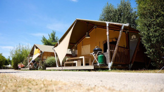 Tienda safari Villatent Nomad en Camping La Roche d’Ully, Francia, con vegetación y cielo azul claro.