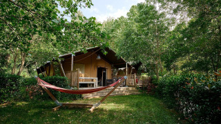 Tienda safari Villatent Nomad en Camping Le Canigou, Francia, rodeada de vegetación y una hamaca.