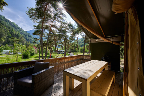 Terraza de madera con mesa y banco, rodeada de pinos y montañas en Camping River, Provence-Alpes-Côte d’Azur.