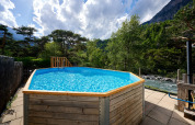 Udendørs swimmingpool med træramme ved Camping River, omgivet af bjerge og træer i Provence-Alpes-Côte d’Azur.