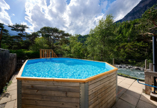 Buitenzwembad met houten rand aan Camping River, gelegen tussen bergen en rivier in Provence-Alpes-Côte d’Azur.