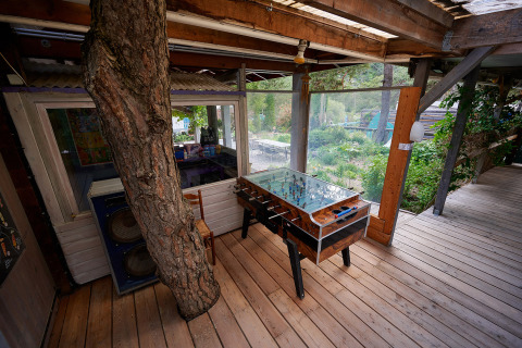 Área de descanso exterior con futbolín y un árbol atravesando el suelo de madera en Camping River, Francia.