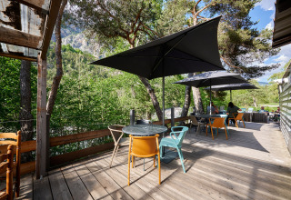 Terrazza all’aperto con tavoli e sedie moderne sotto ombrelloni, immersa nel verde delle Alpi francesi.