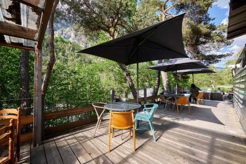 Buitenterras met moderne tafels en stoelen onder zwarte parasols, omgeven door bomen in de Franse Alpen.