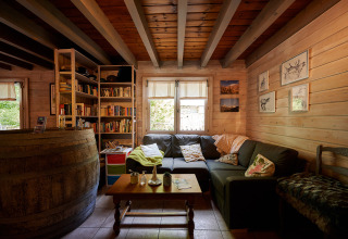 Acogedora sala con paredes de madera, estantería, sofá y mesa en Camping River, Provenza, Francia.