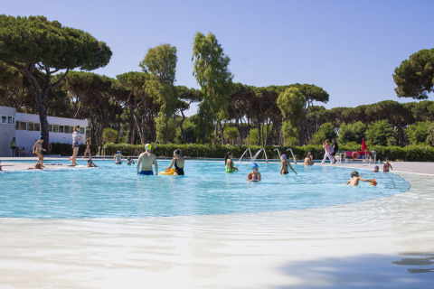 Familias disfrutan en la piscina al aire libre de Camping Roma Capitol en Lazio, Italia, rodeados de árboles.