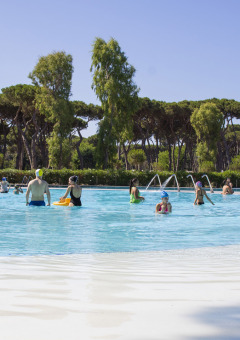 Familias disfrutan en la piscina al aire libre de Camping Roma Capitol en Lazio, Italia, rodeados de árboles.
