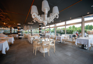 Licht, modern restaurant met grote ramen en witte tafellakens bij Camping Roma Capitol, Lazio, Italië.