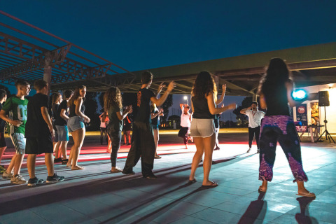 Jóvenes participan en una sesión de baile grupal al aire libre por la noche en Camping Roma Capitol, Lazio, Italia.