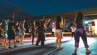 Jóvenes participan en una sesión de baile grupal al aire libre por la noche en Camping Roma Capitol, Lazio, Italia.