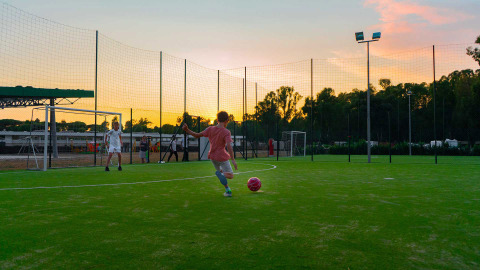 Bambini giocano a calcio al tramonto su un campo al Camping Roma Capitol, un villaggio vacanze nel Lazio, Italia.