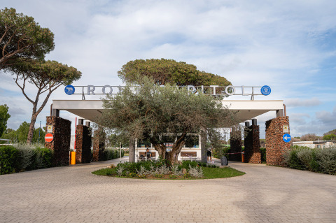 Ingresso di Camping Roma Capitol, villaggio turistico nel Lazio, Italia, con alberi e colonne di pietra ai lati.