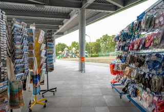 Shop with souvenirs, postcards, and sandals at Camping Roma Capitol holiday park in Lazio, Italy, and playground outside.