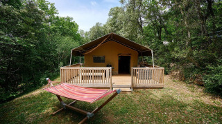 Vista exterior de la tienda safari Villatent Wood con terraza y hamaca en Camping Le Pech Charmant, Francia.