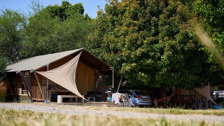 Tienda safari Villatent Nomad en Camping Le Petit Trianon, Francia, rodeada de árboles y un coche al lado.