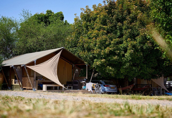 Tienda safari Villatent Nomad en Camping Le Petit Trianon, Francia, rodeada de árboles y un coche al lado.