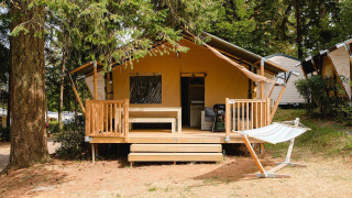Acogedora cabaña Villatent Outback con porche y hamaca, rodeada de árboles en Camping Le Sequoia, Francia.