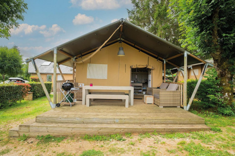 Tienda safari Villatent Nomad con terraza de madera y zona de estar exterior en Camping Les Genêts, Francia.