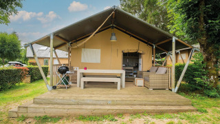 Tienda safari Villatent Nomad con terraza de madera y zona de estar exterior en Camping Les Genêts, Francia.