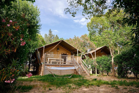 Tienda safari Villatent Nomad en Camping Les Pêcheurs en Francia, rodeada de árboles y flores brillantes.