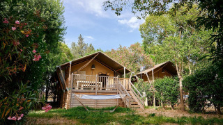 Safari tent Villatent Nomad op Camping Les Pêcheurs in Frankrijk, omgeven door bomen en kleurrijke planten.