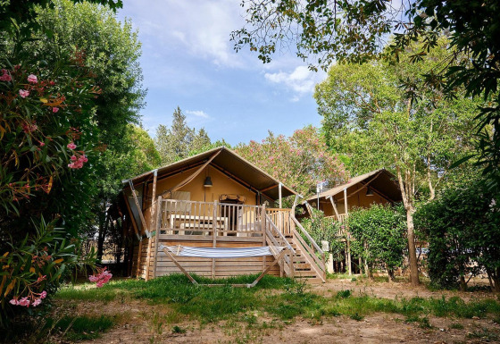Tienda safari Villatent Nomad en Camping Les Pêcheurs en Francia, rodeada de árboles y flores brillantes.