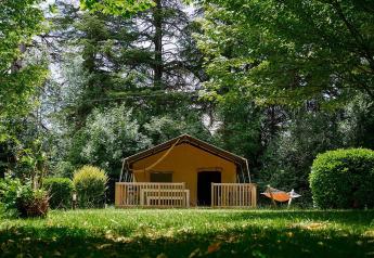 Safari tent Villatent Wood at Camping Lestaubière in France, surrounded by green trees and a hammock.