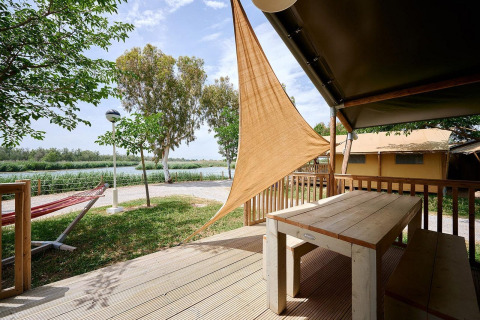 Vista desde la terraza de una tienda safari con mesa de madera en Camping Nautic Almata, junto a la naturaleza.