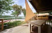 View from a safari tent deck with wooden table at Camping Nautic Almata, featuring hammock and nature.