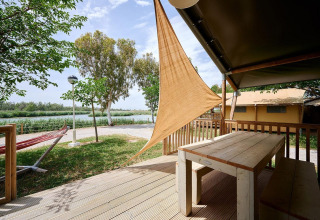 Vista dal terrazzo di una tenda safari con tavolo in legno al Camping Nautic Almata, con amaca e natura.