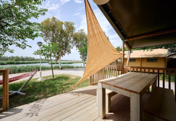 Vue depuis la terrasse d’une tente safari avec table en bois au Camping Nautic Almata, hamac et verdure.