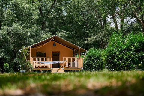 Tienda safari Villatent Nomad en Camping Lestaubière, Francia, rodeada de árboles verdes y una hamaca al frente.