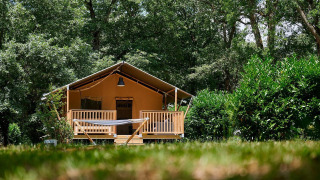 Tienda safari Villatent Nomad en Camping Lestaubière, Francia, rodeada de árboles verdes y una hamaca al frente.
