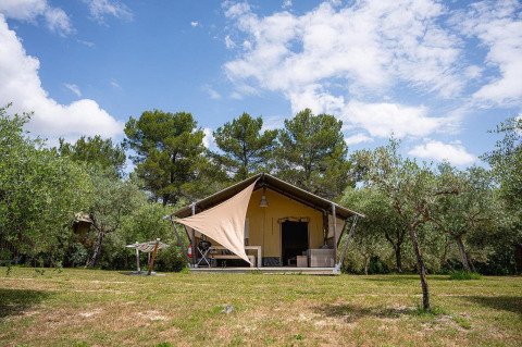 Tienda safari Villatent Nomad en Camping Pian Di Boccio, Italia, rodeada de árboles y cielo azul.