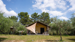 Tienda safari Villatent Nomad en Camping Pian Di Boccio, Italia, rodeada de árboles y cielo azul.