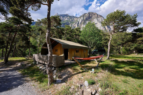Tienda safari Villatent Wood en Camping River, Francia, rodeada de árboles, césped y montañas al fondo.