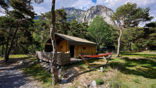 Safari-telt ved Camping River i Frankrig, omgivet af træer, græsareal og bjerge i baggrunden.