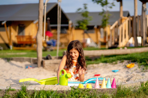 Meisje speelt in een zandbak met speelgoed bij FarmCamps Hoeve Luyterheyde vakantiepark, Noord-Brabant, Nederland.