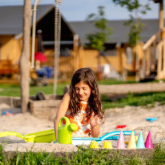 Pige leger i sandkasse med legetøj på FarmCamps Hoeve Luyterheyde, et feriepark i Nordbrabant, Holland.