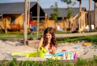 Bambina gioca con giocattoli da sabbia nella sabbiera a FarmCamps Hoeve Luyterheyde, parco vacanze nel Brabante Settentrionale, Paesi Bassi.