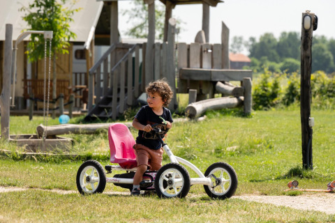 Un niño monta en un kart de pedales sobre el césped cerca del parque en FarmCamps Hoeve Luyterheyde, Holanda.