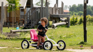 Et barn kører på en pedalbil på græsset ved legeområdet på FarmCamps Hoeve Luyterheyde i Holland.