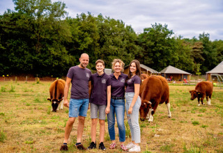 Familie på FarmCamps Hoeve Luyterheyde i Nordbrabant, Nederlandene, med køer og feriehytter i baggrunden.