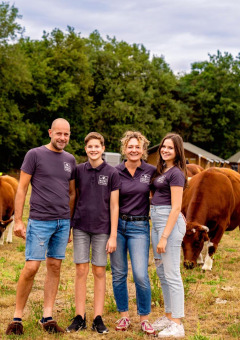 Familie på FarmCamps Hoeve Luyterheyde i Nordbrabant, Nederlandene, med køer og feriehytter i baggrunden.