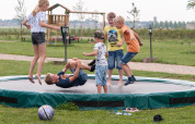 Børn leger på en stor trampolin på FarmCamps Op Flakkee feriepark i Sydholland, Holland, omgivet af natur.